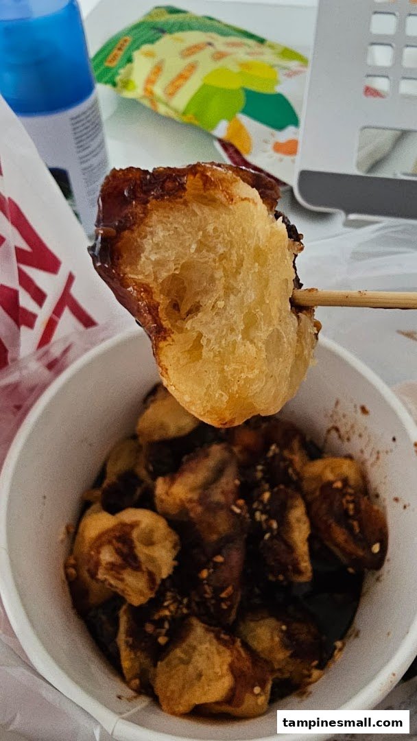 A close-up of a fried dough stick (youtiao) dipped in chocolate sauce with nuts, served in a cup.