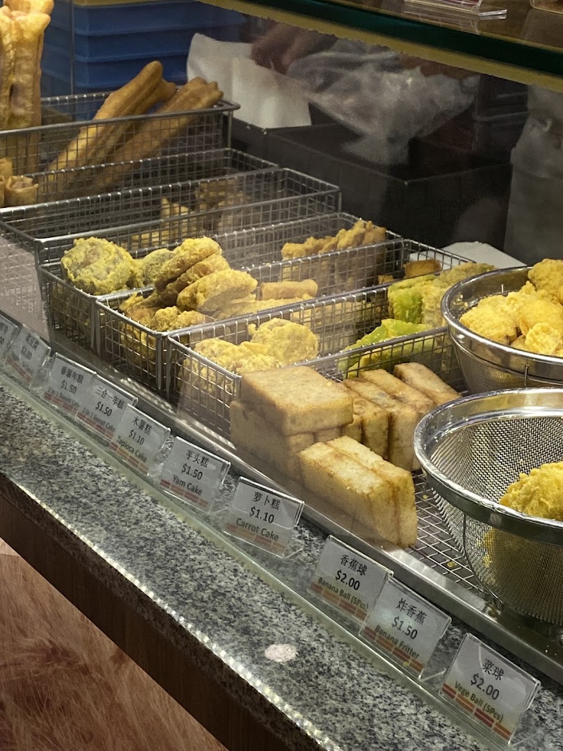 A vibrant display of freshly fried snacks and traditional cakes with clear pricing at Dough Culture.