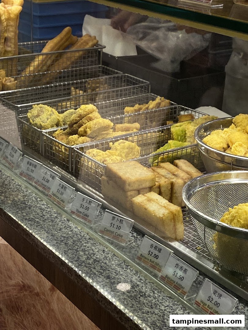 A vibrant display of freshly fried snacks and traditional cakes with clear pricing at Dough Culture.