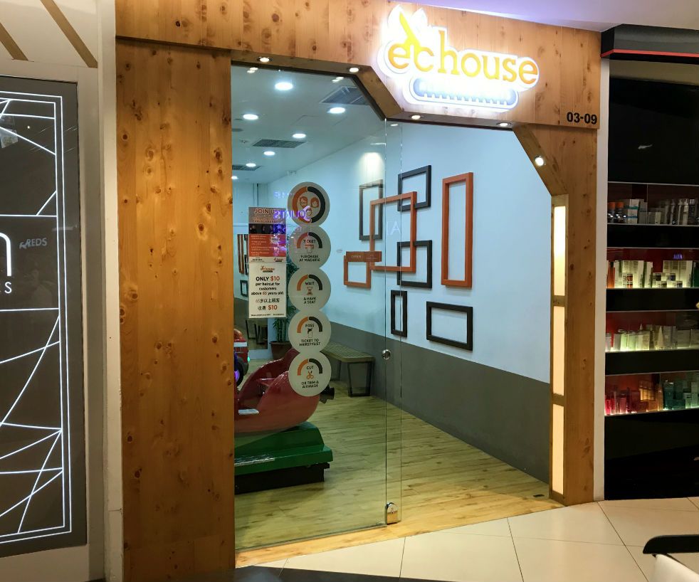 The inviting wooden entrance of EC House, a hair salon, featuring a clear glass door and signage.