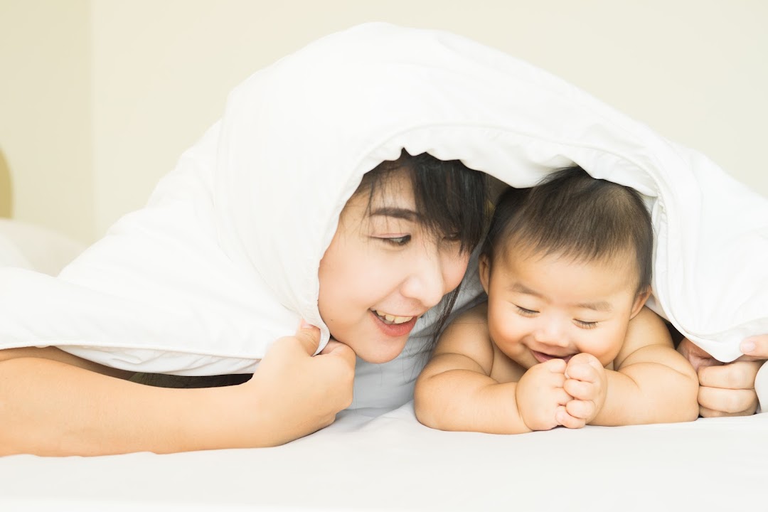 A mother and baby smiling under a white blanket, symbolizing comfort and family moments.