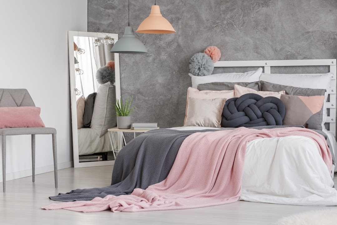 A stylish bedroom display featuring a bed with pink and grey bedding, decorative pillows, and modern decor.