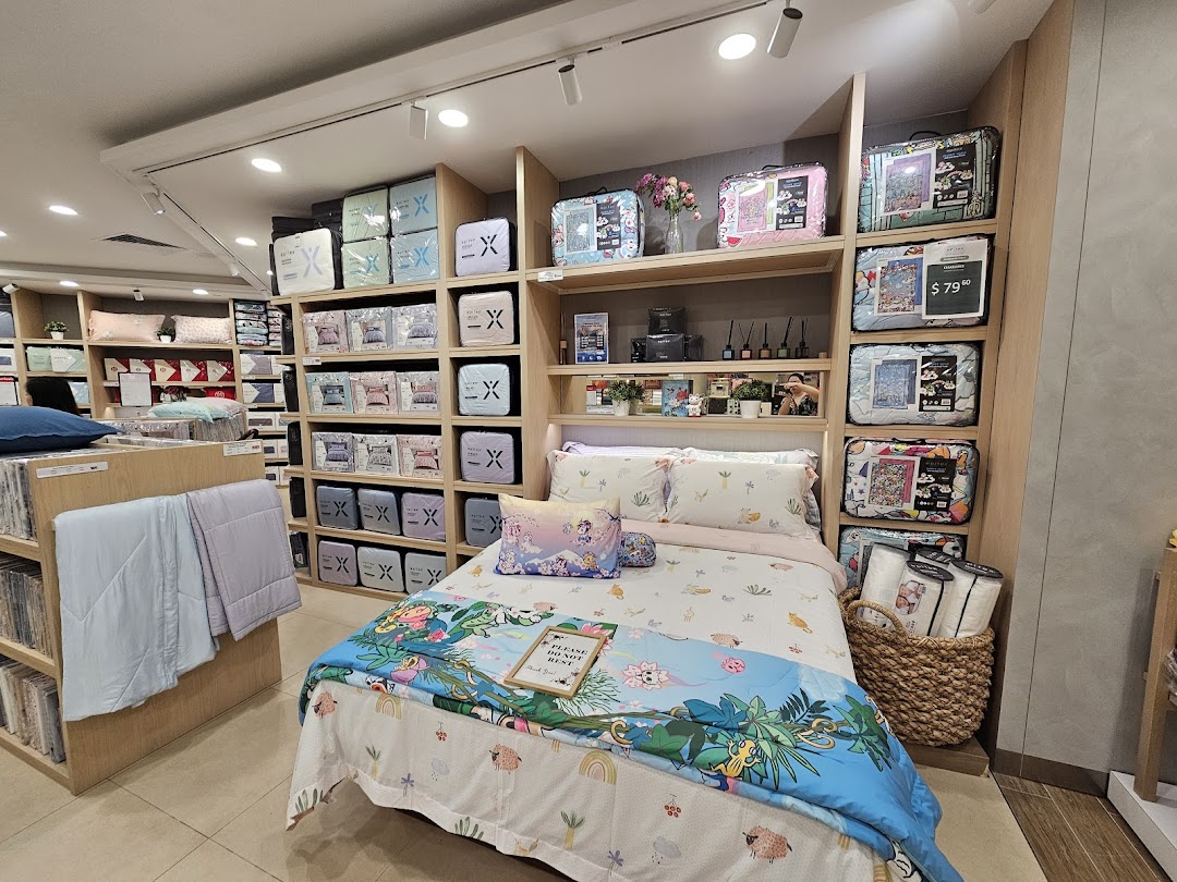 An interior view of Epitex, showcasing a vibrant display bed and shelves filled with bedding and linen products.