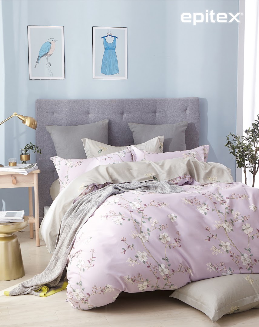 A beautifully styled bed featuring lavender floral bedding, grey pillows, and a tufted headboard.