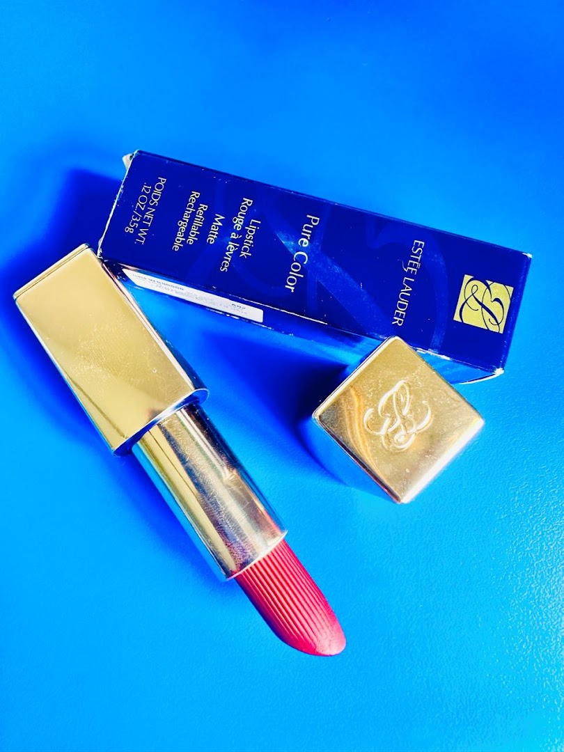 An Estée Lauder Pure Color lipstick in a gold case with its blue product box on a blue background.