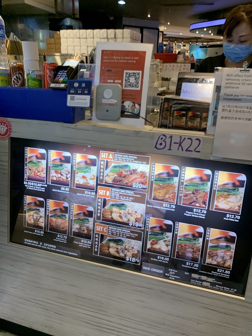 A digital menu board at Express Teppan-Yaki, showcasing various set meals and prices, with a staff member at the counter.