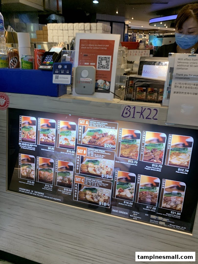 A digital menu board at Express Teppan-Yaki, showcasing various set meals and prices, with a staff member at the counter.