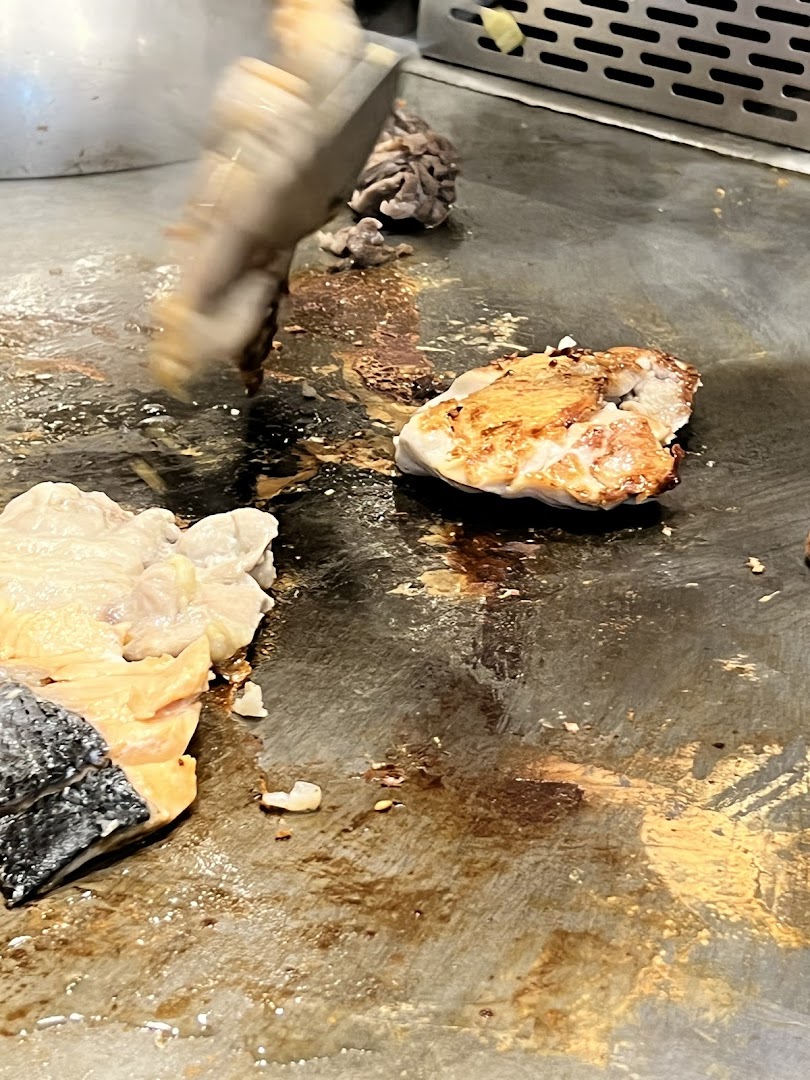 Close-up of chicken and salmon cooking on a sizzling teppanyaki grill with a spatula.