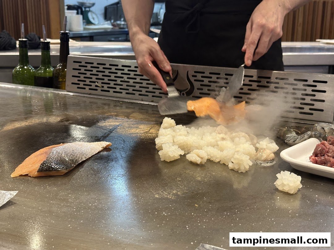 A chef expertly cooks fresh seafood and meat on a sizzling teppan grill.