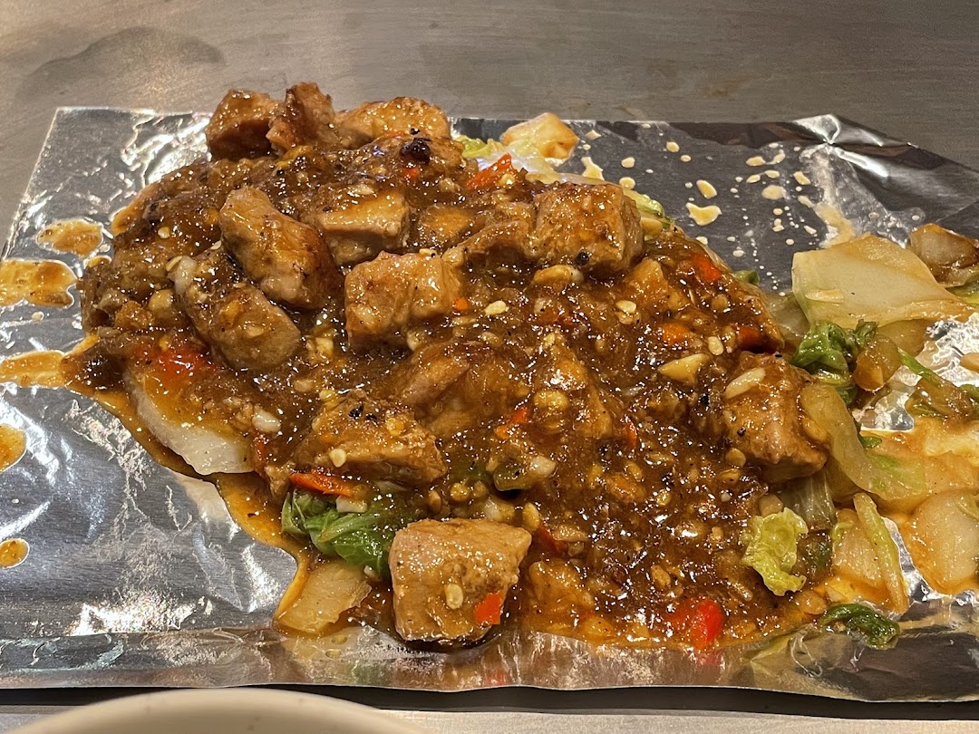 A close-up of a savory teppanyaki dish featuring saucy meat cubes and vegetables on foil.
