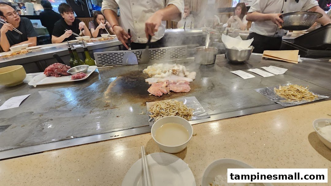 A chef prepares fresh ingredients on a sizzling teppanyaki grill for seated customers.