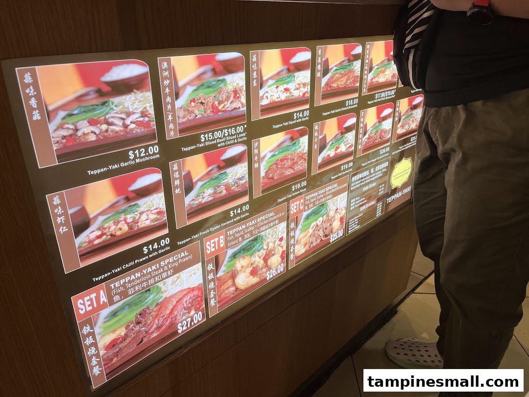 A brightly lit menu display showcasing various Teppan-Yaki dishes with prices and images.