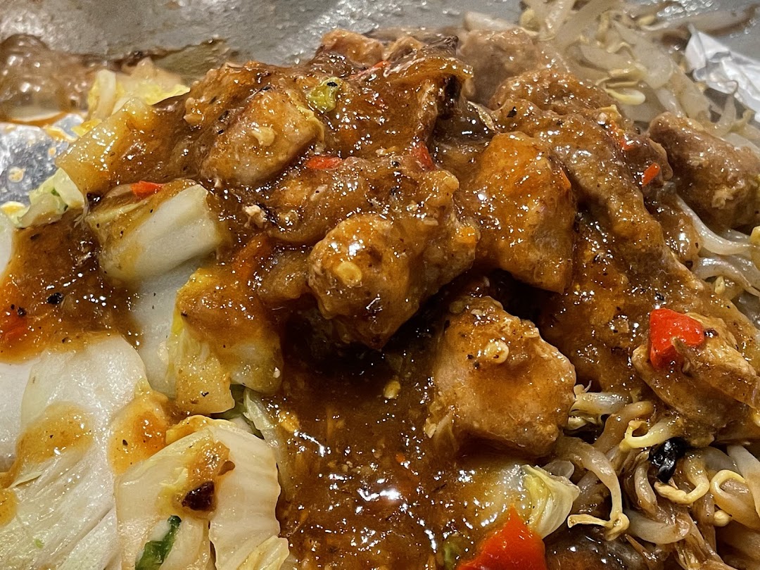 Close-up of sizzling teppanyaki chicken and vegetables coated in a rich, savory sauce.