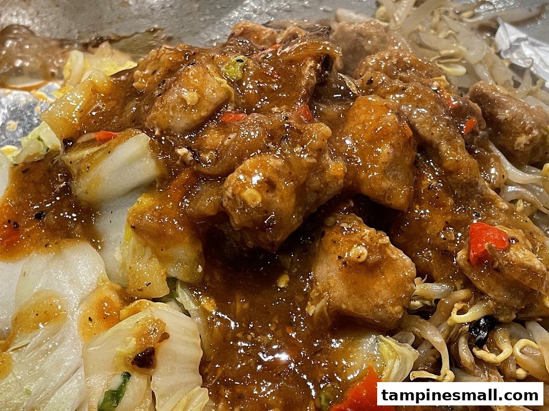 Close-up of sizzling teppanyaki chicken and vegetables coated in a rich, savory sauce.