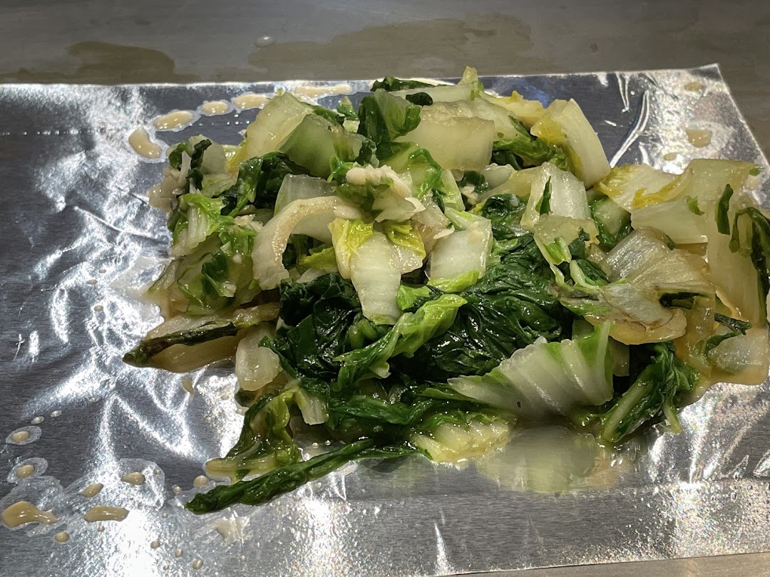 Freshly cooked green vegetables, likely bok choy, served on aluminum foil from a teppanyaki grill.