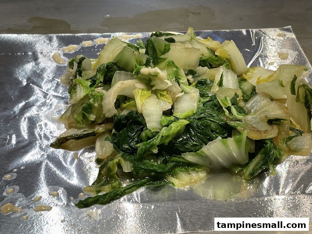 Freshly cooked green vegetables, likely bok choy, served on aluminum foil from a teppanyaki grill.