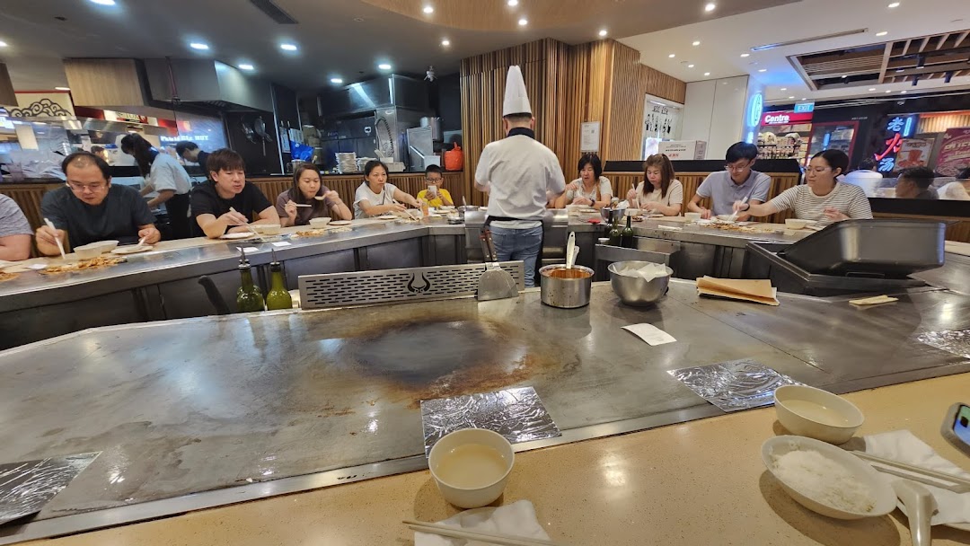 Diners enjoy a lively teppanyaki experience with a chef cooking fresh ingredients on a large grill.