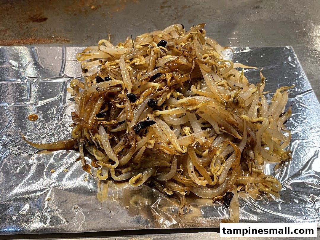 Close-up of stir-fried bean sprouts served on foil, fresh from a teppanyaki grill.