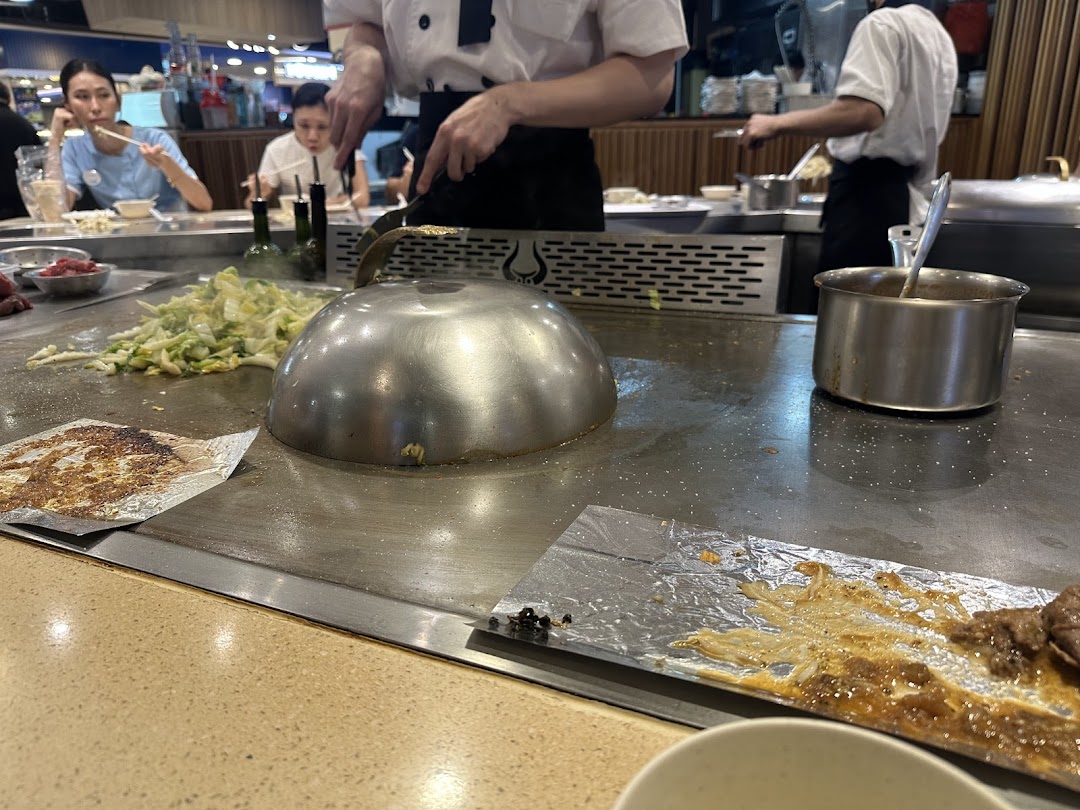 A chef cooks teppanyaki dishes on a hot griddle for customers at Express Teppan-Yaki.