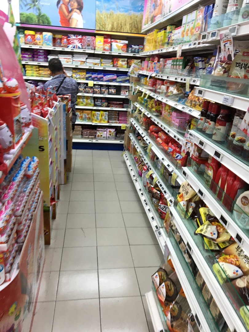 An interior view of a FairPrice supermarket aisle, showcasing well-stocked shelves with various packaged goods and a shopper.