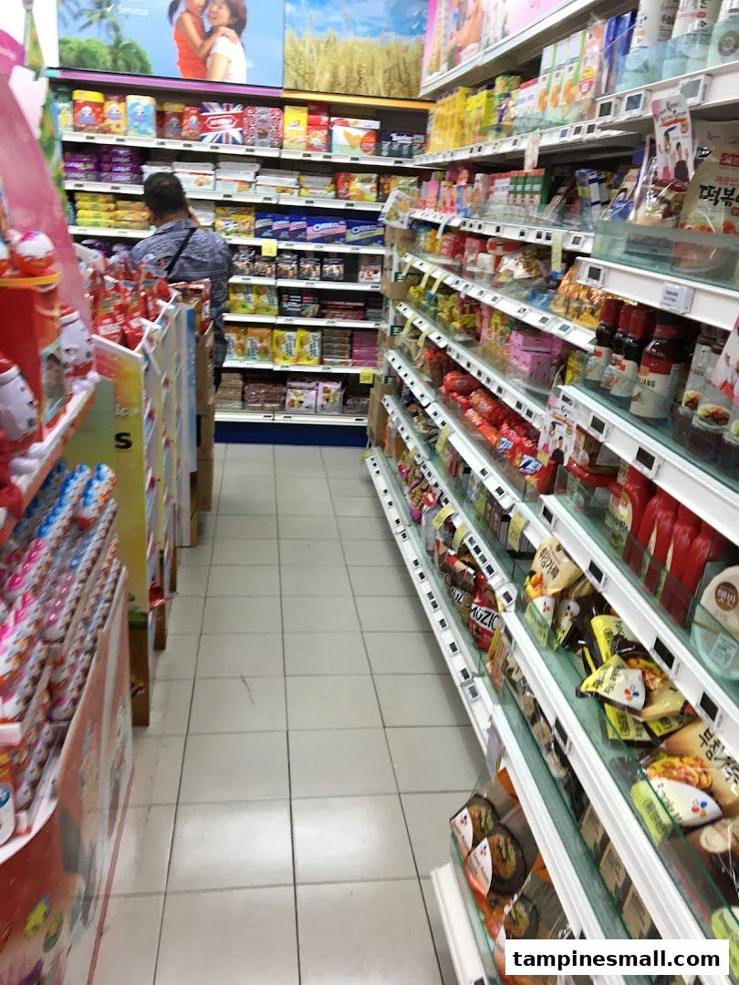 An interior view of a FairPrice supermarket aisle, showcasing well-stocked shelves with various packaged goods and a shopper.