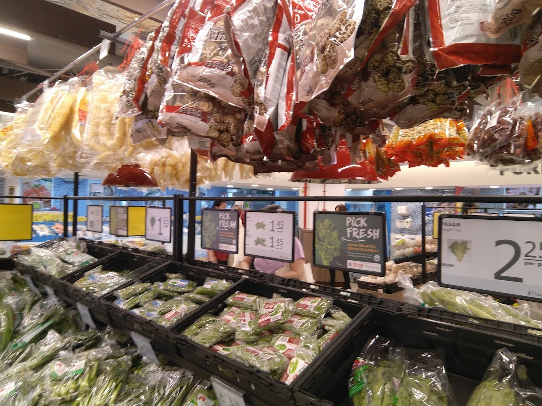 A vibrant fresh produce section at FairPrice, featuring packaged vegetables, leafy greens, and hanging dried goods.