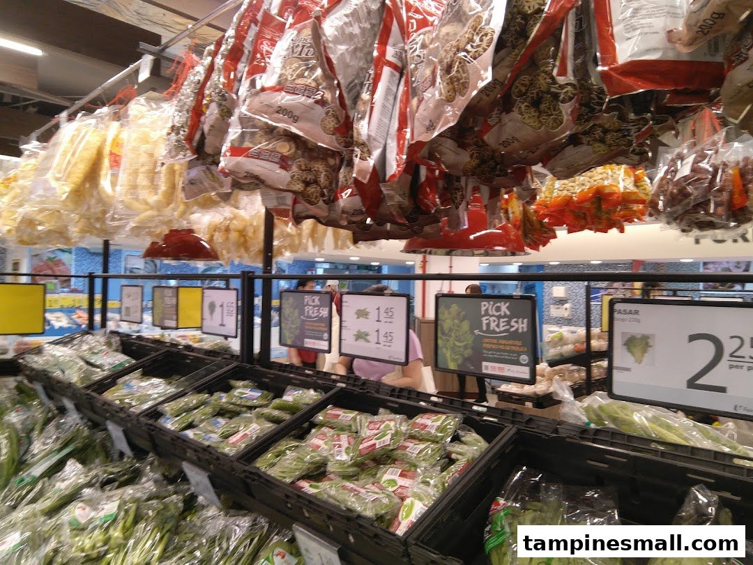 A vibrant fresh produce section at FairPrice, featuring packaged vegetables, leafy greens, and hanging dried goods.