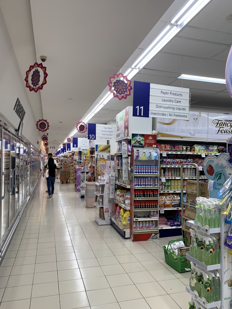 A wide, well-lit aisle inside FairPrice supermarket, showcasing various household products and a customer.