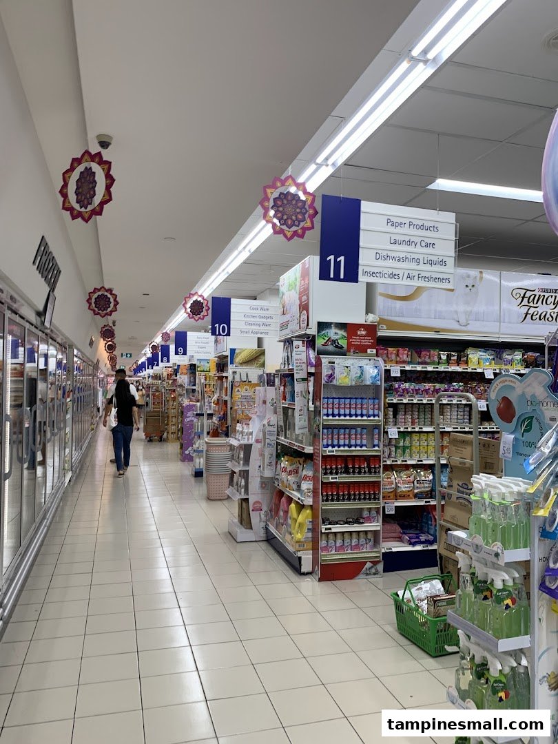A wide, well-lit aisle inside FairPrice supermarket, showcasing various household products and a customer.