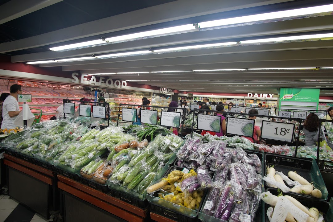 A bustling supermarket aisle at FairPrice Tampines Mall, featuring a wide array of fresh vegetables and produce.