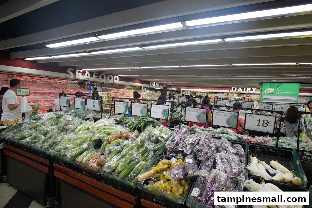 A bustling supermarket aisle at FairPrice Tampines Mall, featuring a wide array of fresh vegetables and produce.