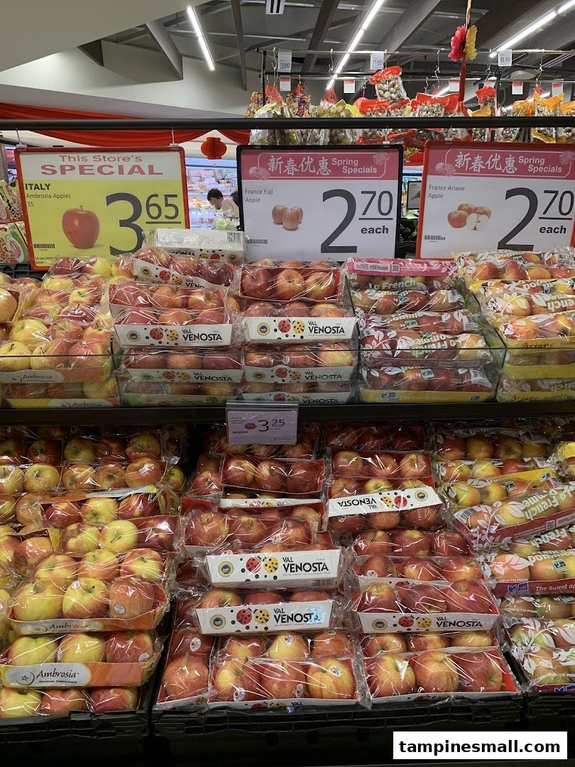 A vibrant display of various packaged apples with special offer signs at FairPrice Tampines Mall.