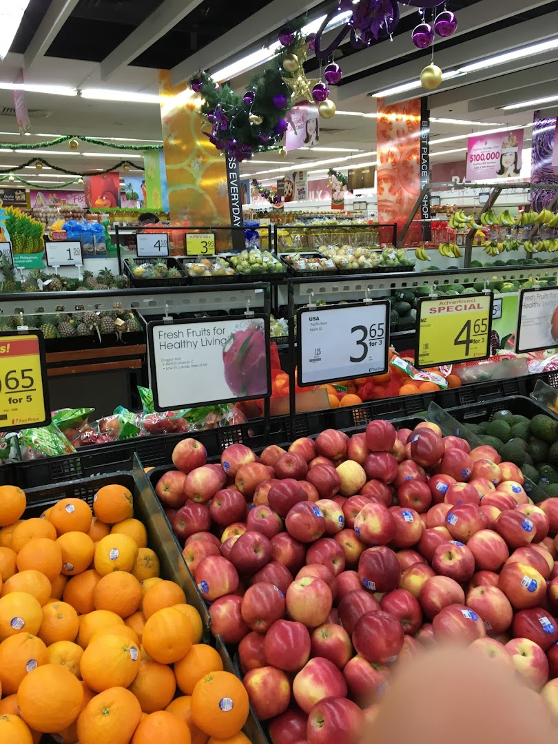Vibrant display of fresh oranges and apples in a FairPrice supermarket aisle, featuring produce promotions.