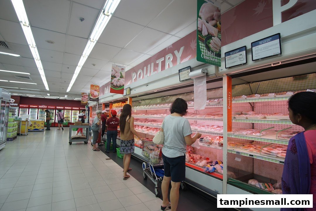 Shoppers browse fresh poultry and meat selections in a well-stocked supermarket aisle.