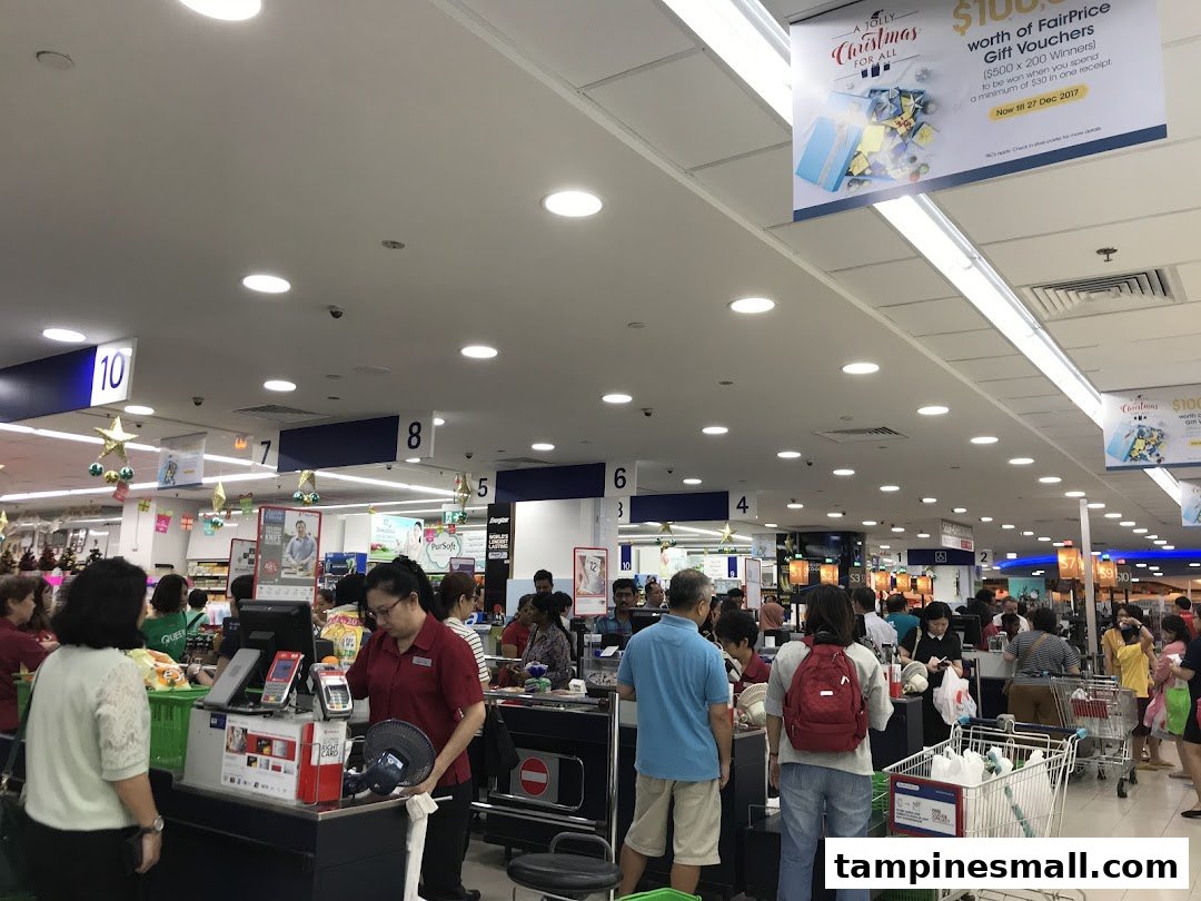 Busy checkout area of a FairPrice supermarket with customers and cashiers.