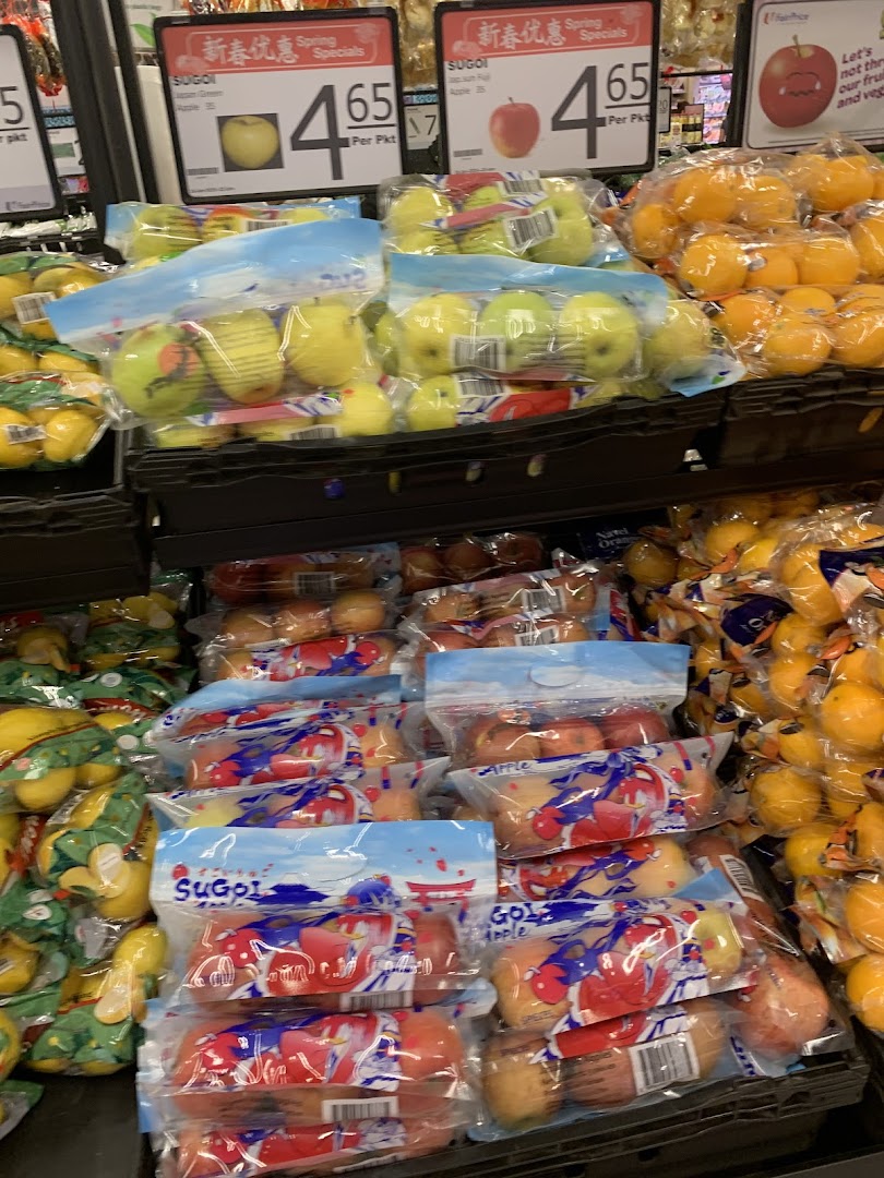 Packaged apples and citrus fruits displayed for sale with price signs in a supermarket.