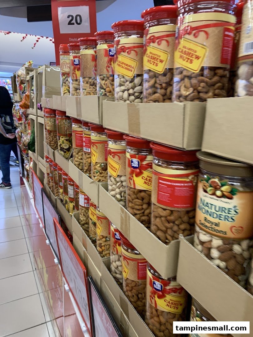 An aisle display at FairPrice Tampines Mall featuring various nuts and dried fruits in jars, including cashews and pistachios.