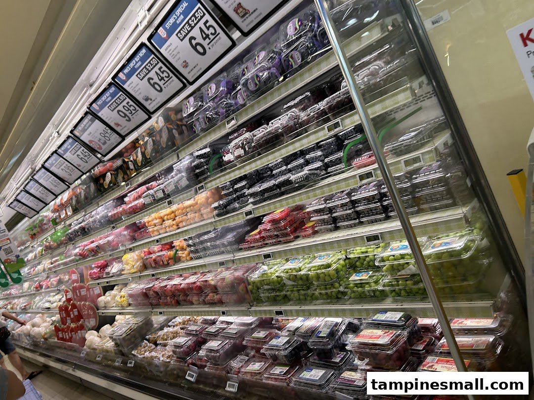 A refrigerated display case showcasing a wide variety of fresh fruits and vegetables at FairPrice Tampines Mall.