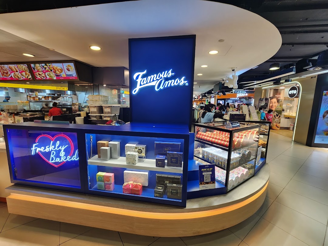 An interior view of Famous Amos, showcasing its counter, 'Freshly Baked' neon sign, and cookie displays.