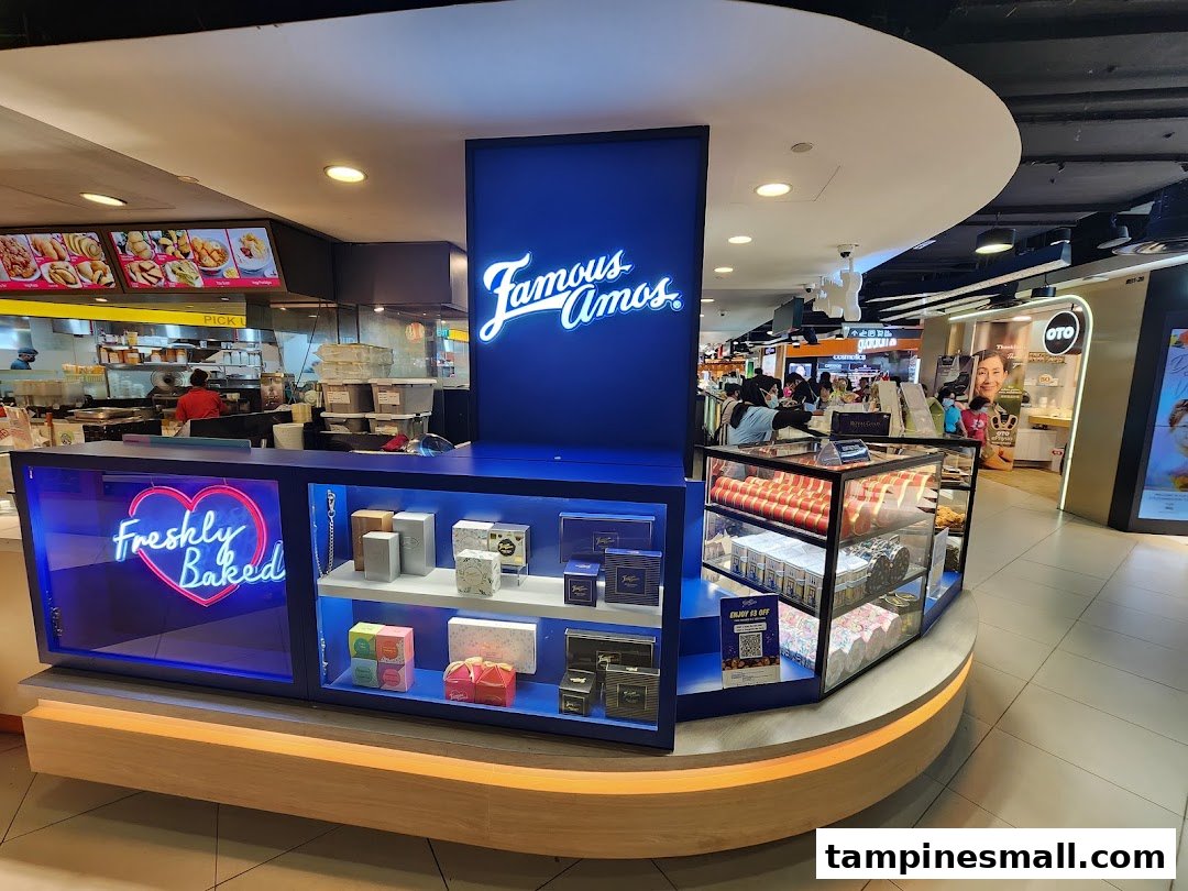 An interior view of Famous Amos, showcasing its counter, 'Freshly Baked' neon sign, and cookie displays.
