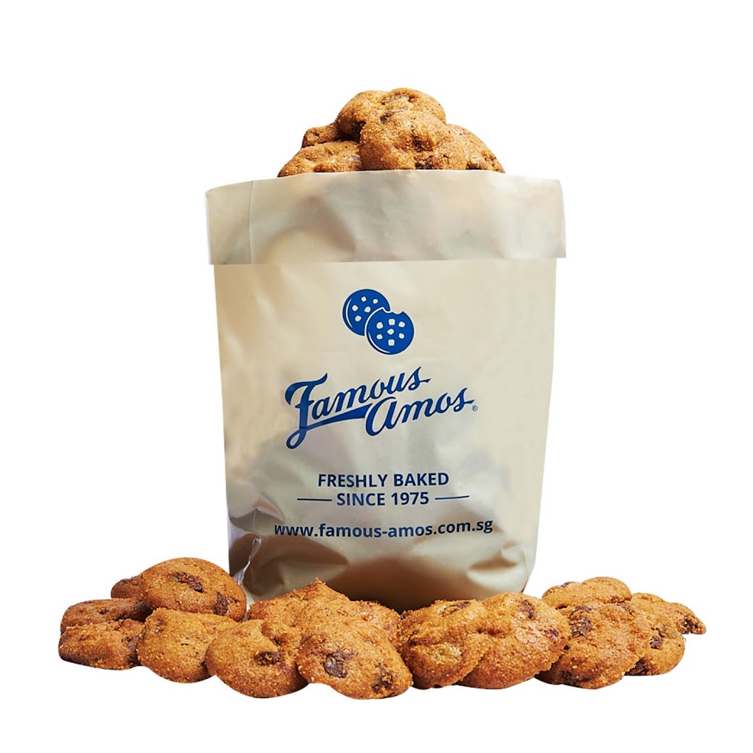 Famous Amos bag filled with freshly baked chocolate chip cookies, with more cookies scattered.