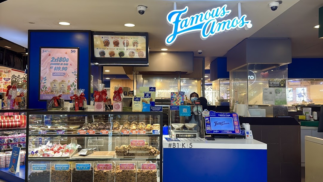 A vibrant interior view of Famous Amos, showcasing fresh cookies, gift sets, and the service counter.