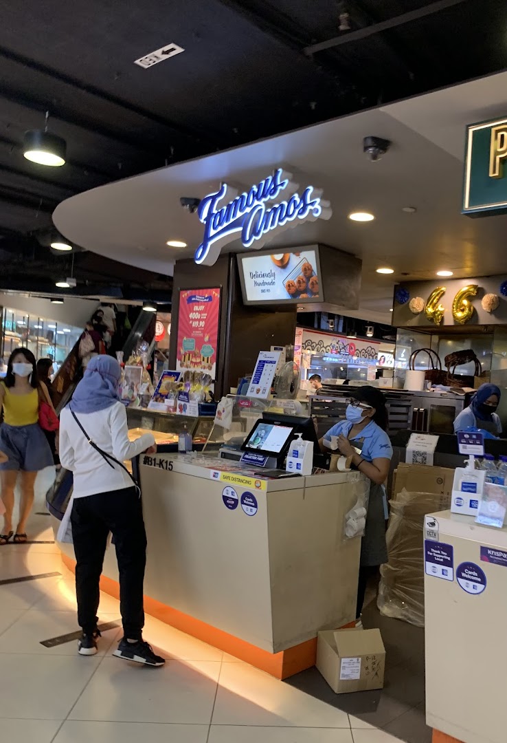 A customer at the Famous Amos counter, with staff preparing orders in a bustling mall setting.