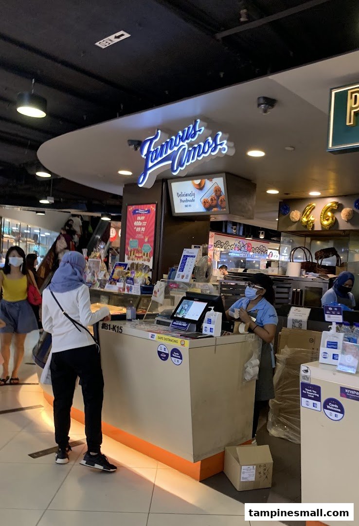 A customer at the Famous Amos counter, with staff preparing orders in a bustling mall setting.