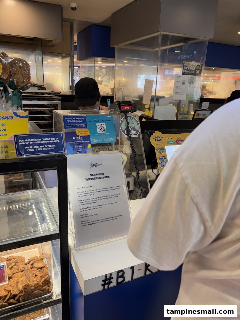 A bustling Famous Amos counter with a staff member, fresh cookies on display, and various payment signs.
