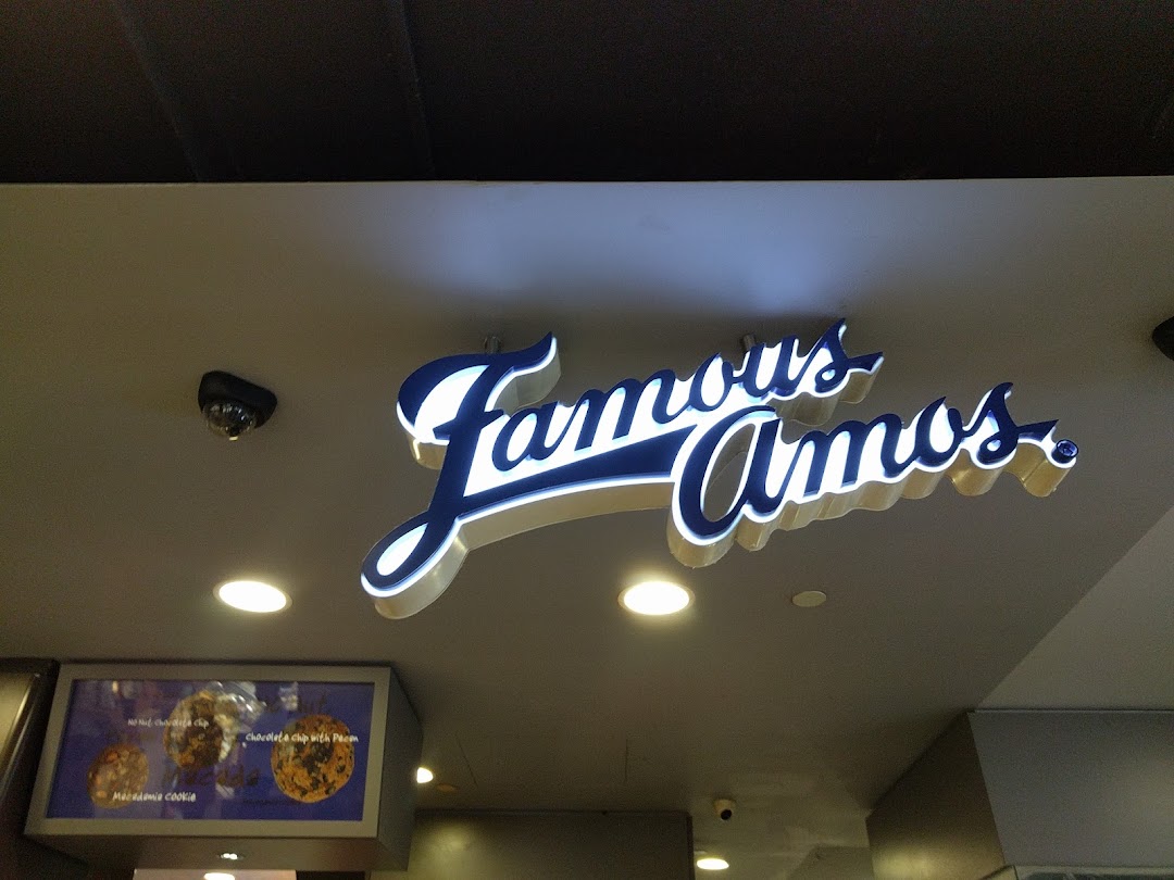 An illuminated 'Famous Amos' sign above a display showcasing various cookie flavors.