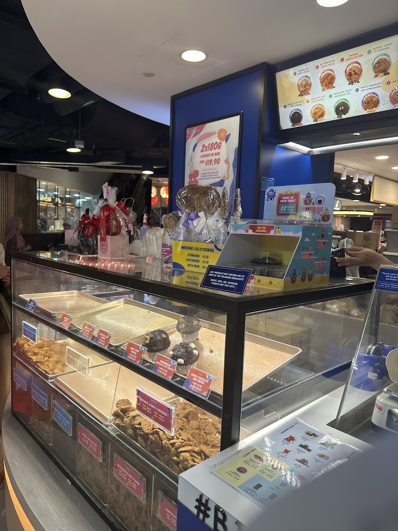 A display counter at Famous Amos showcasing various cookies, muffins, and promotional offers.