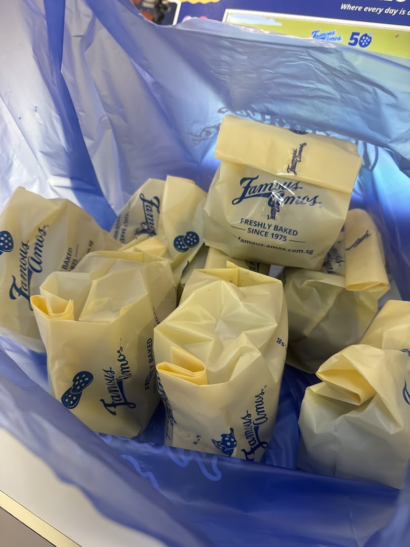 Multiple Famous Amos cookie bags, freshly baked, are seen inside a blue shopping bag.
