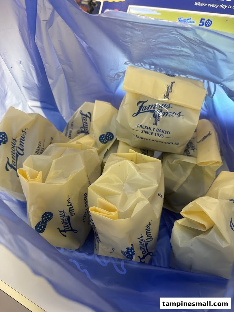Multiple Famous Amos cookie bags, freshly baked, are seen inside a blue shopping bag.