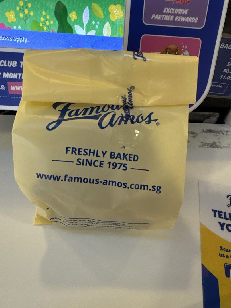 A yellow Famous Amos cookie bag displaying its logo, 'Freshly Baked Since 1975', and website.